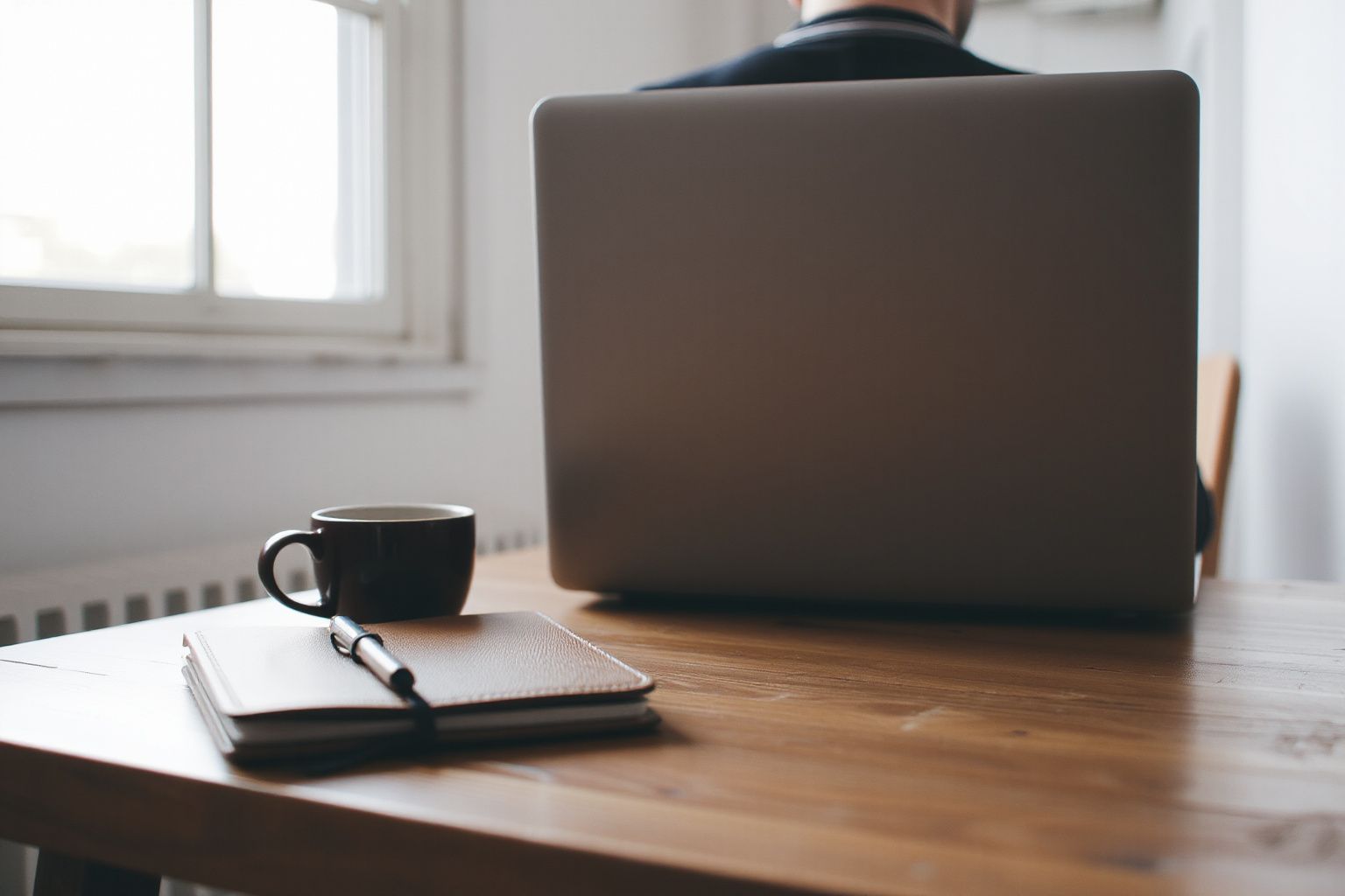 Canada eTA Approval Email Explained: person sitting at a wooden desk looking at a laptop, with a coffee mug and notebook nearby