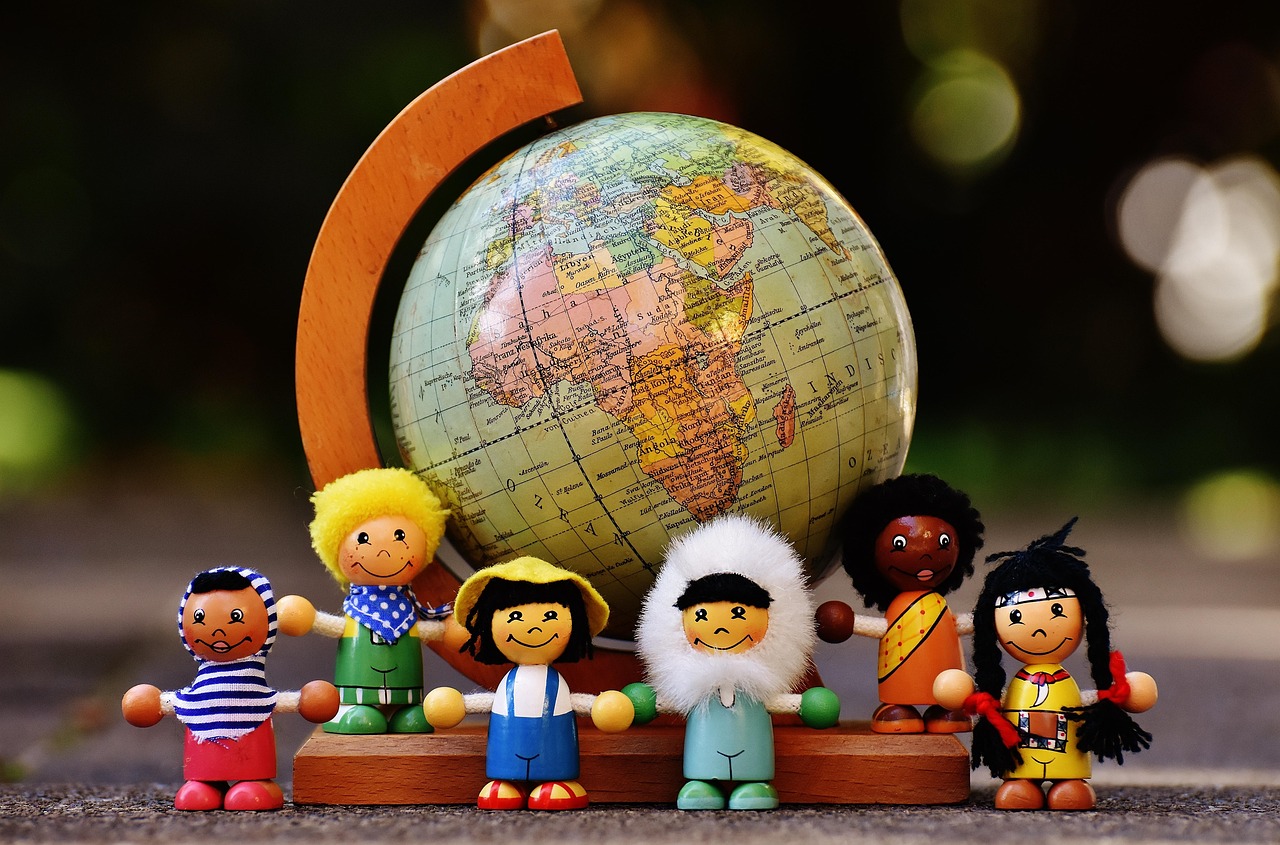 Six diverse wooden dolls holding hands in front of a small globe showing continents.