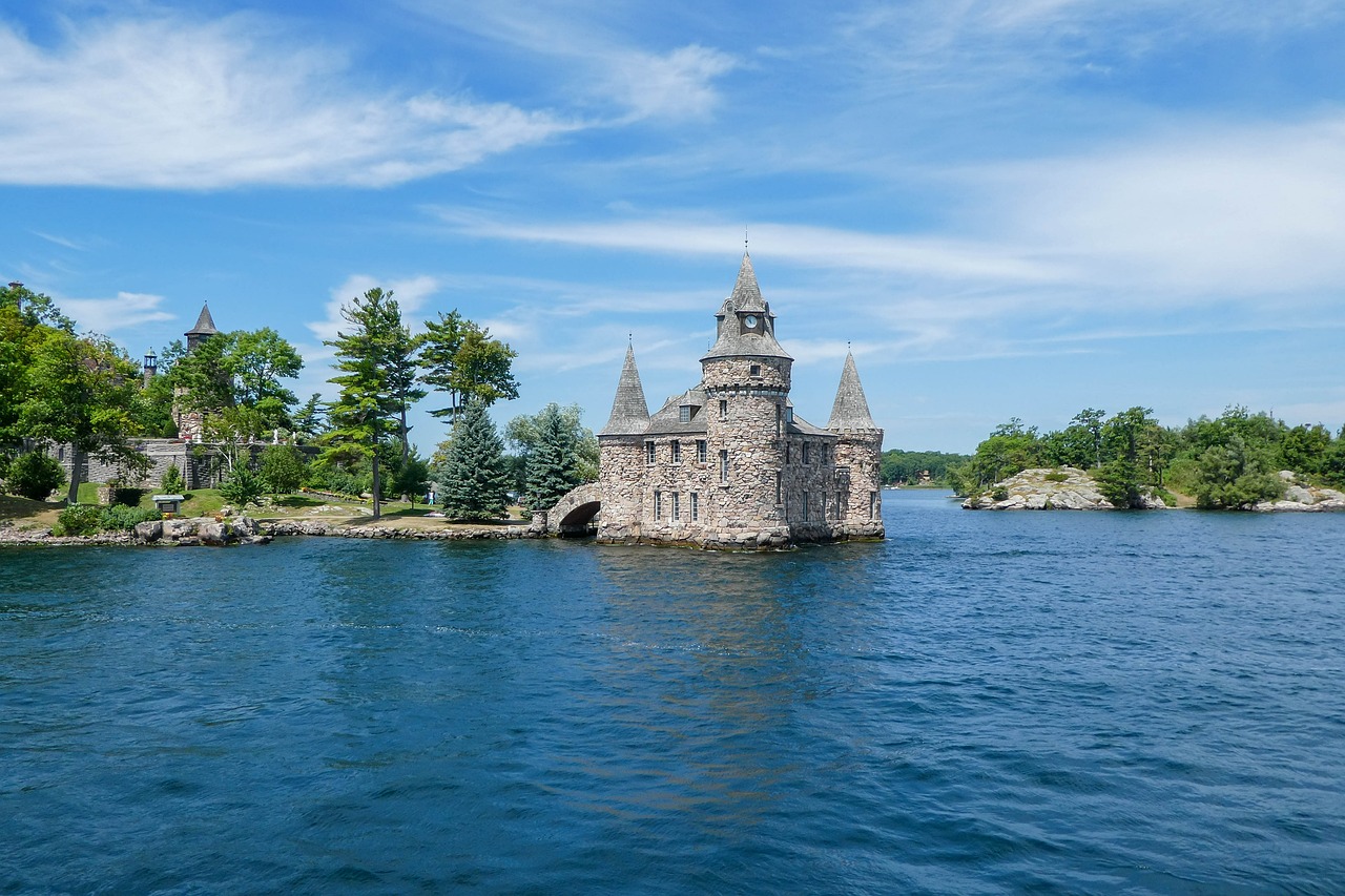 A stone castle with turrets and a clock tower stands on an island in a body of water.