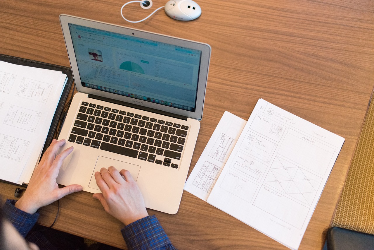 eTA Application, More Information Needed: overhead view of a person working on a laptop with wireframe sketches on a desk