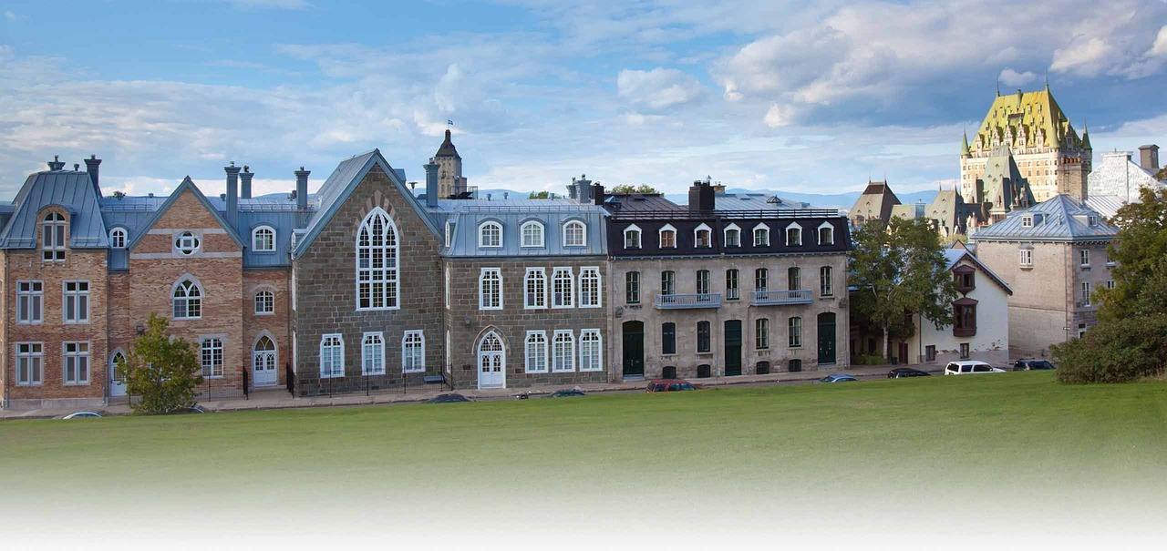 Historic buildings and a grassy slope with a chateau-style hotel in the background under a partly cloudy sky.