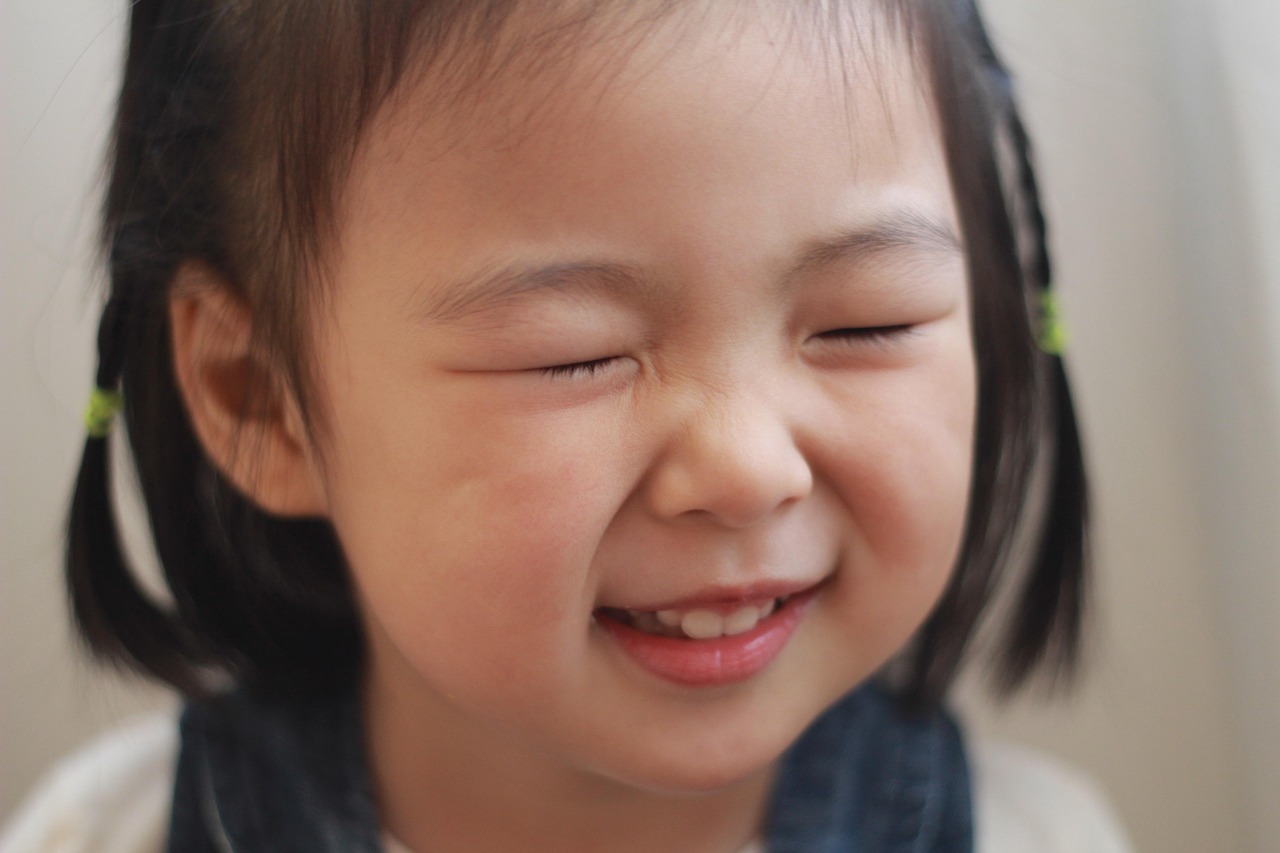 Close-up of a young child smiling with eyes closed, with dark hair in pigtails.