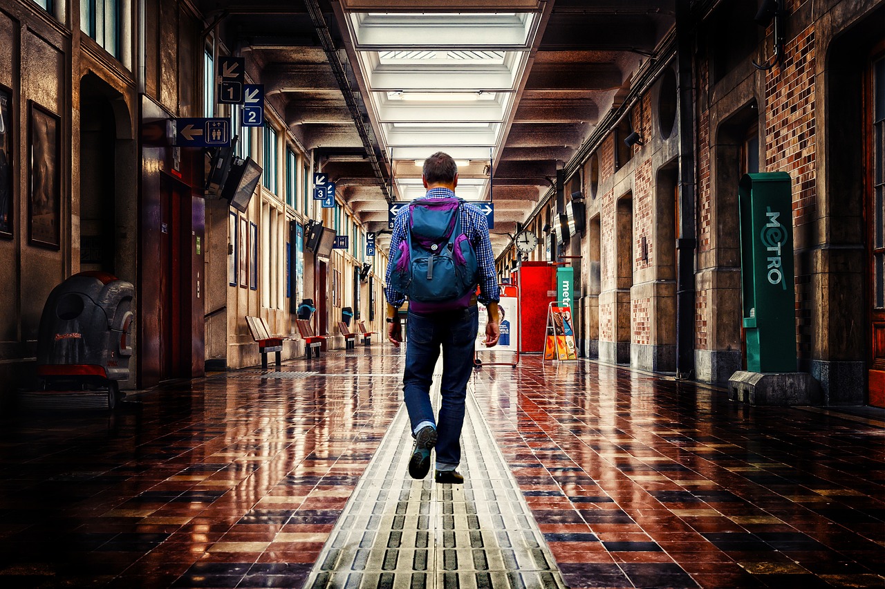 Person with a backpack walking down a long, tiled hallway in a station.