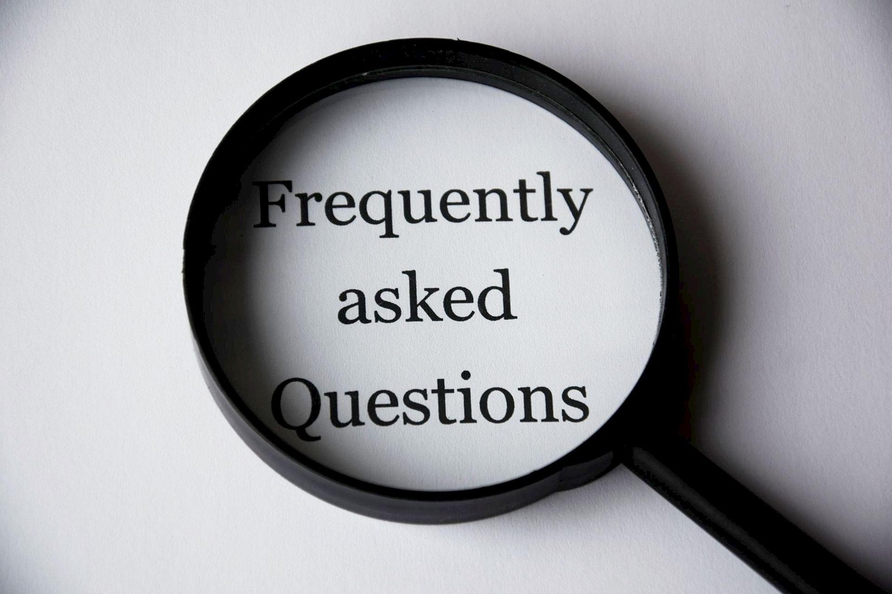 A magnifying glass magnifies the words ‘Frequently asked Questions’ on a white surface.